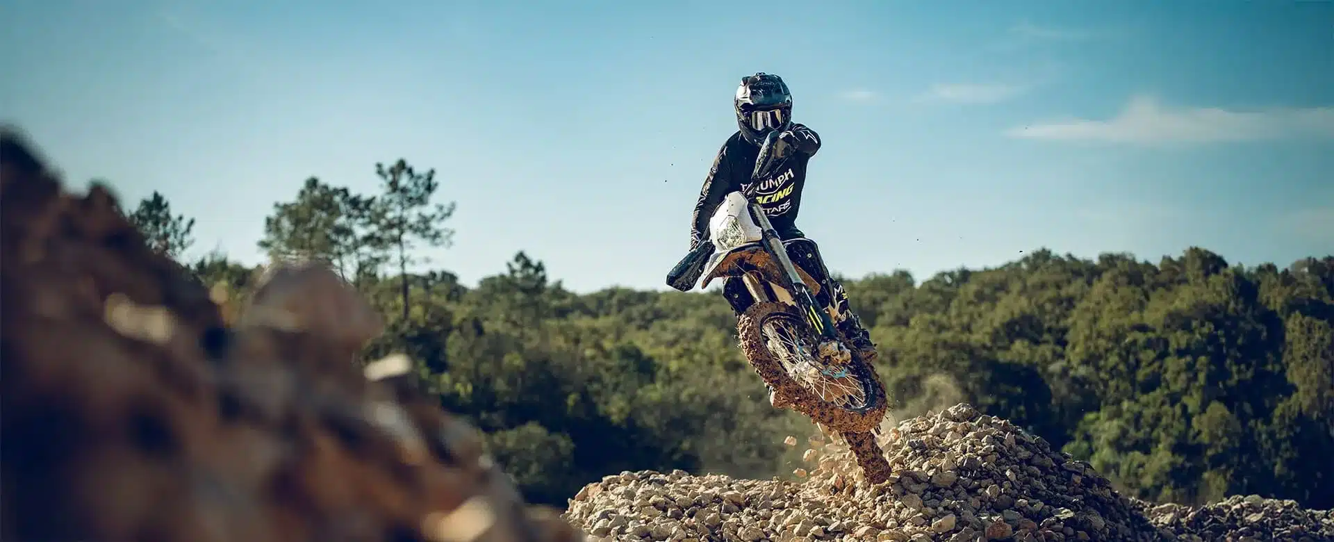 Ein Fahrer auf der Triumph TF 450-E fährt im Gelände über einen steinigen Untergrund.