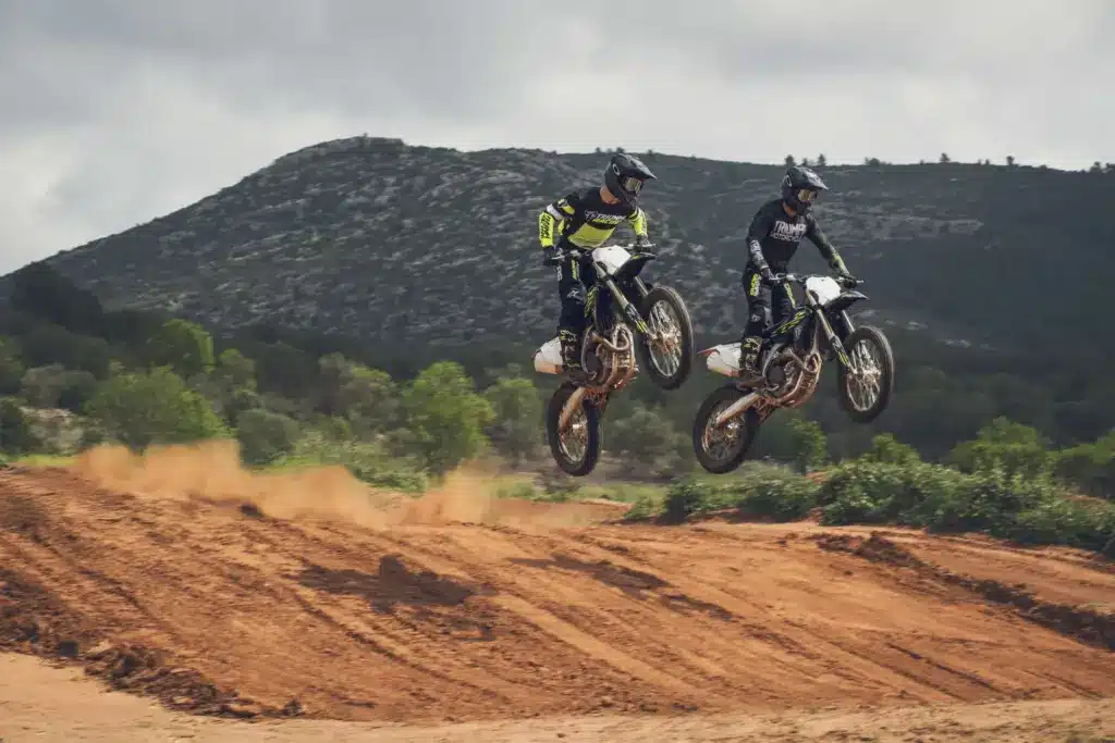 Zwei Triumph TF 450-X Motocross-Motorräder mit Fahrern in voller Ausrüstung beim Sprung auf einer Offroad-Strecke.