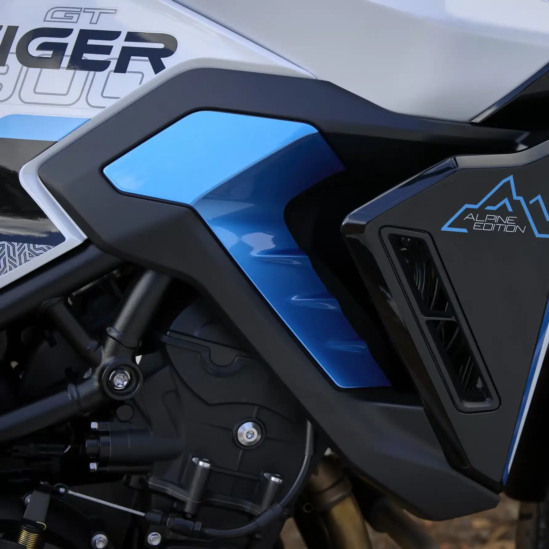Nahaufnahme des Seitenteils der Triumph Tiger 900 Alpine Edition, das das Alpine Edition Logo und die blau-schwarze Verkleidung zeigt.