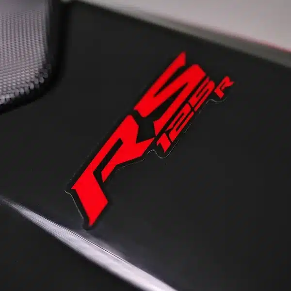 RS 125 R Logo in Rot auf schwarzem Motorradteil, Detailansicht