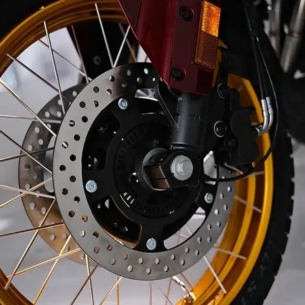 Nahaufnahme des Vorderrads mit goldener Felge, Bremsscheibe und Bremsanlage der SWM Versante 550