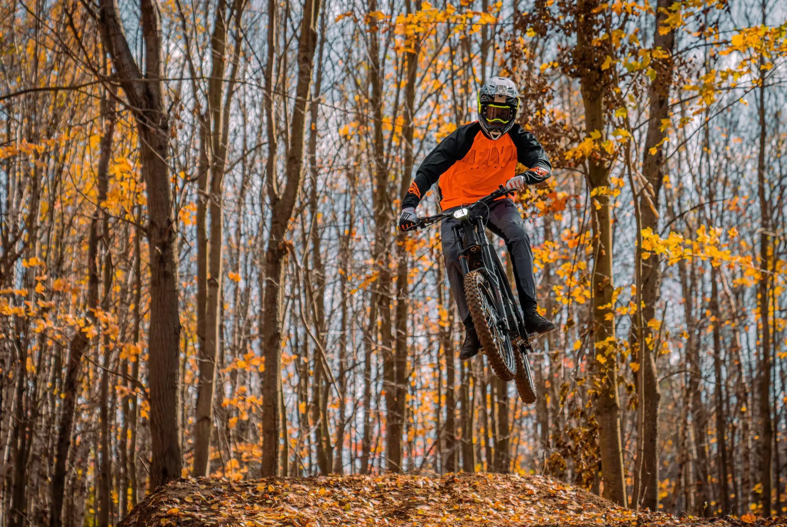 Talaria Sting MX3 Elektro-Dirtbike beim Sprung im Wald mit Fahrer in Schutzkleidung