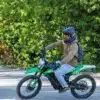 Person fährt eine grüne Rieju e-Tango Elektro-Enduro auf einer Straße, umgeben von Bäumen