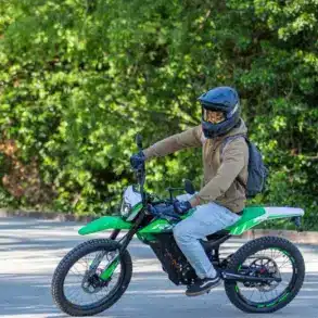 Person fährt eine grüne Rieju e-Tango Elektro-Enduro auf einer Straße, umgeben von Bäumen
