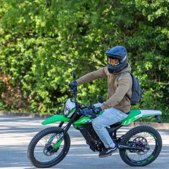Person fährt eine grüne Rieju e-Tango Elektro-Enduro auf einer Straße, umgeben von Bäumen