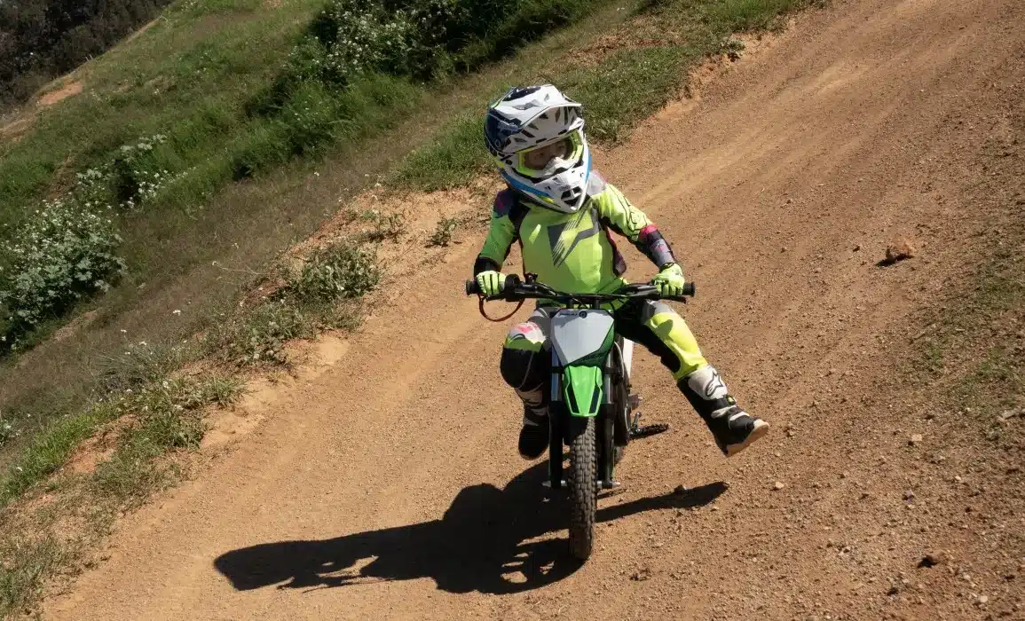 Kind auf grün-weißer Rieju MX12 250W Elektromotocross-Maschine auf einer staubigen Offroad-Strecke