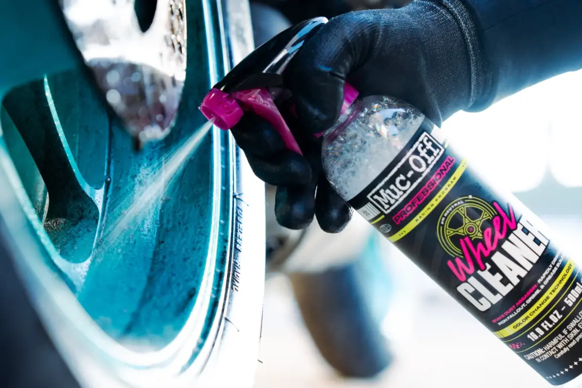 Sprühflasche mit Motorradfelgenreiniger wird auf eine verschmutzte Felge aufgetragen