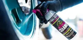Sprühflasche mit Motorradfelgenreiniger wird auf eine verschmutzte Felge aufgetragen