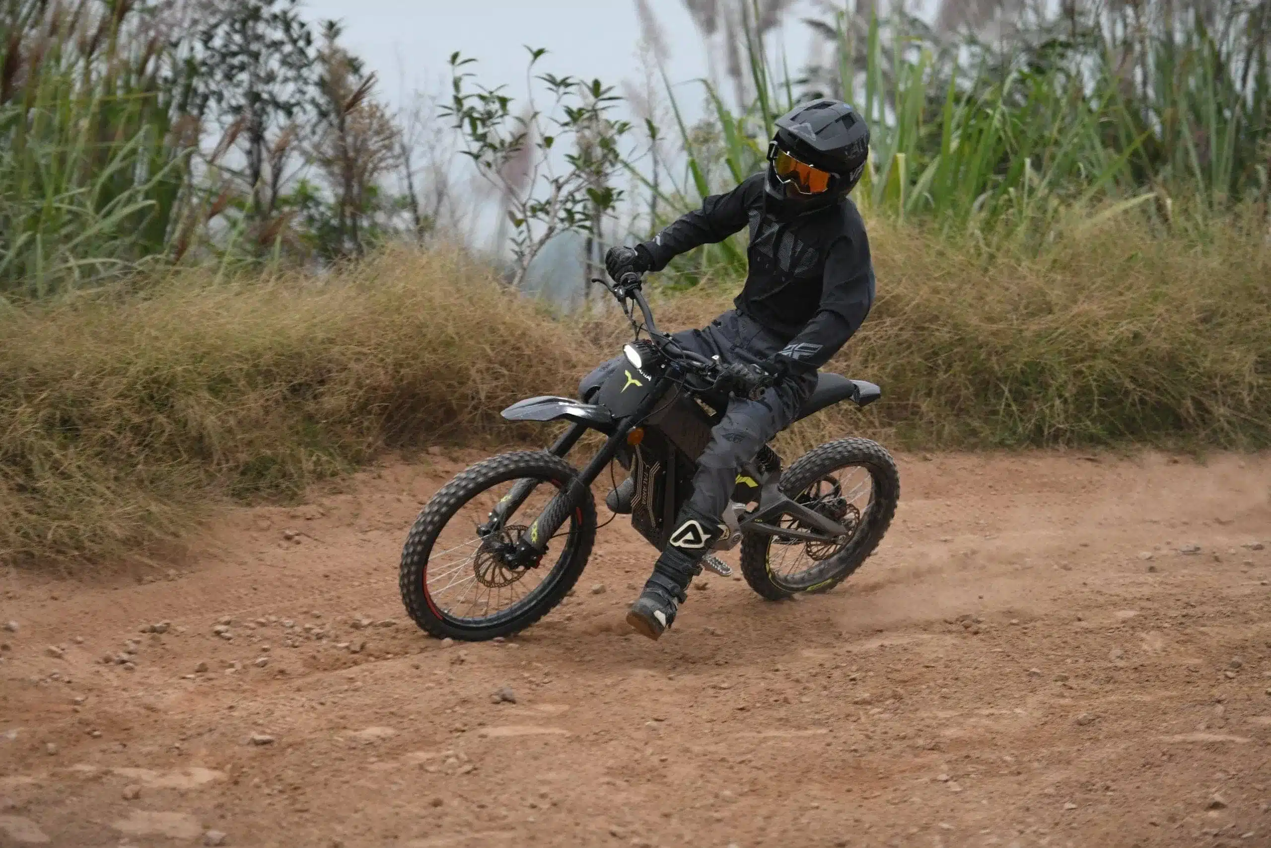 Fahrer auf einer schwarzen Talaria X3 Concept Electric Dirt Bike auf einem Offroad-Pfad.