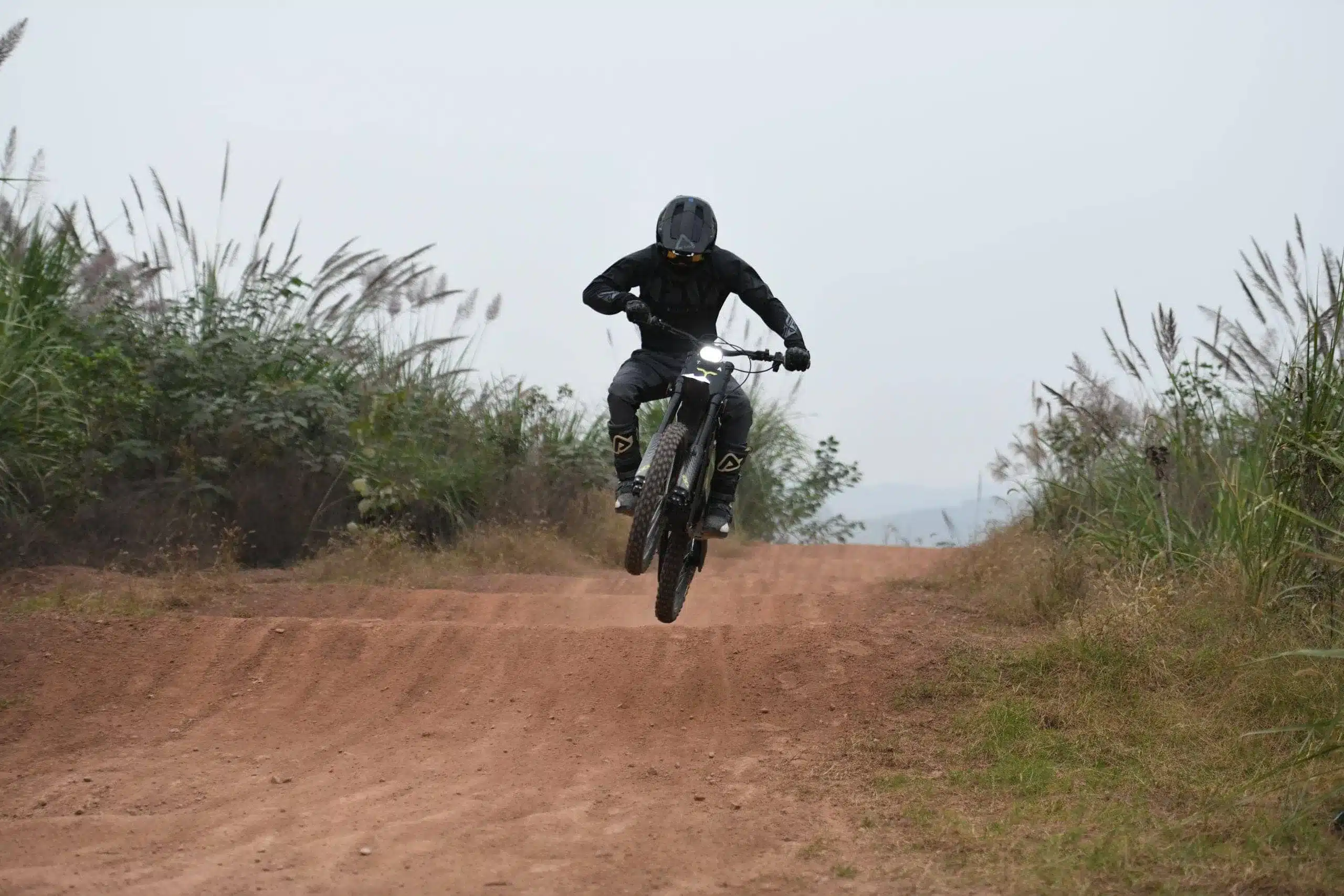 Eine Talaria X3 Concept Electric Dirt Bike beim Sprung auf einer Offroad-Strecke mit Fahrer in schwarzer Schutzkleidung.