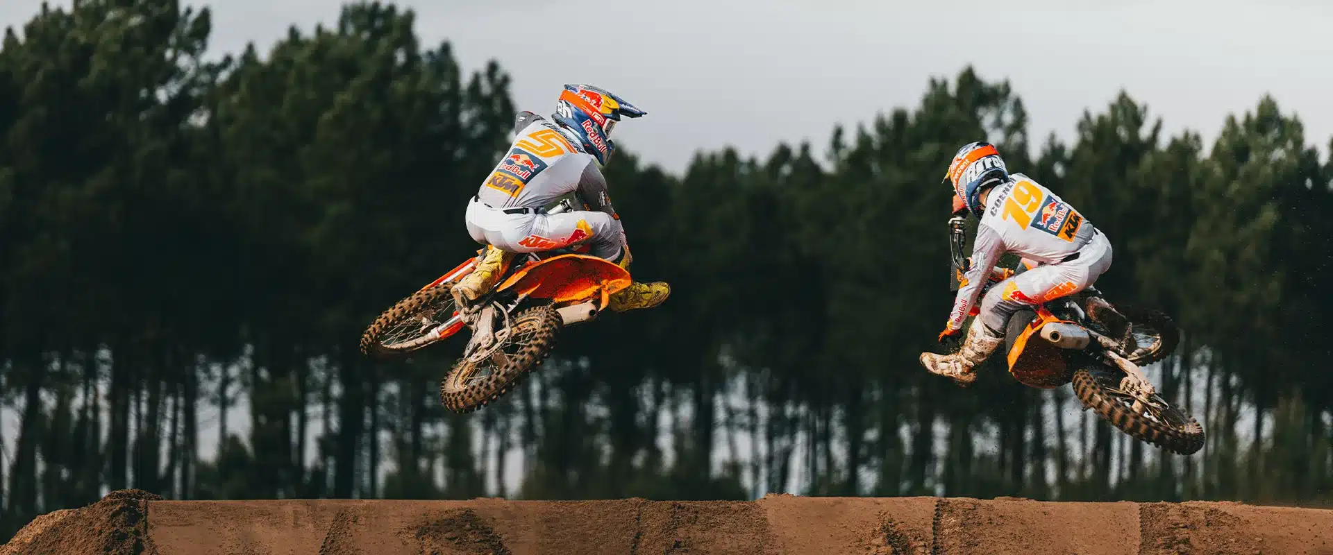 Zwei Motocross-Fahrer auf KTM 250 SX Motorrädern beim Sprung auf einer Offroad-Strecke vor Wald.