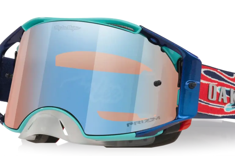 Oakley Airbrake MX Troy Lee Designs White Blue Stars mit reflektierendem Prizm MX Low Light Glas und verstellbarem, rot-blau gemustertem Band.