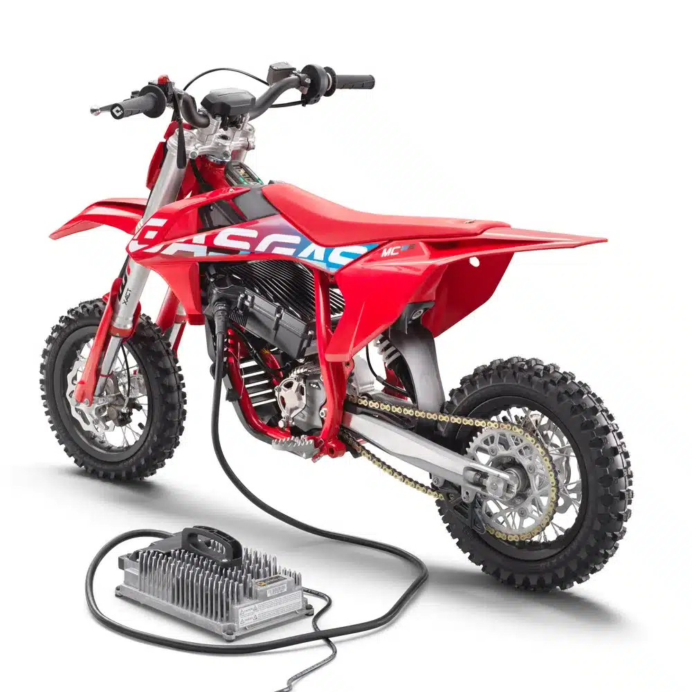 Detailaufnahme der GASGAS MC-E 3 2024 als Elektro-Kindermotocross mit Ladegerät und grobstolligen Reifen.