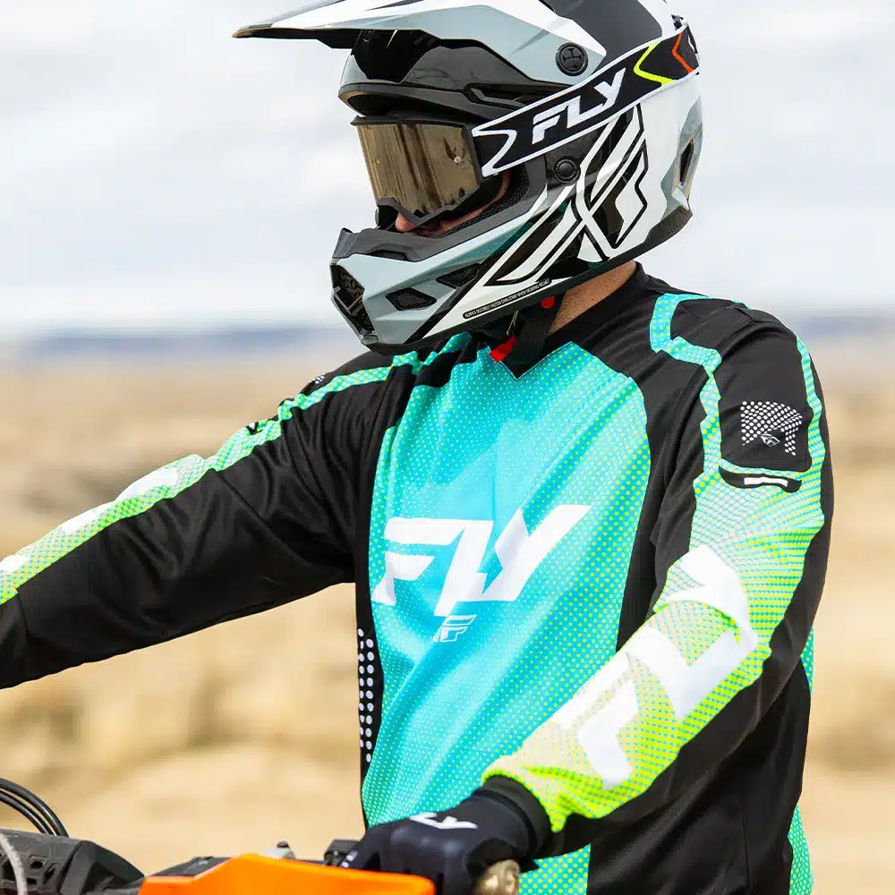 Motorradfahrer trägt ein Fly Racing F-16 Jersey in Türkis, Schwarz und Gelb sowie einen passenden Helm