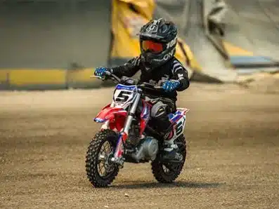 Junges Kind mit Schutzkleidung fährt ein RFZ Dirt Bike 70cc auf losem Untergrund