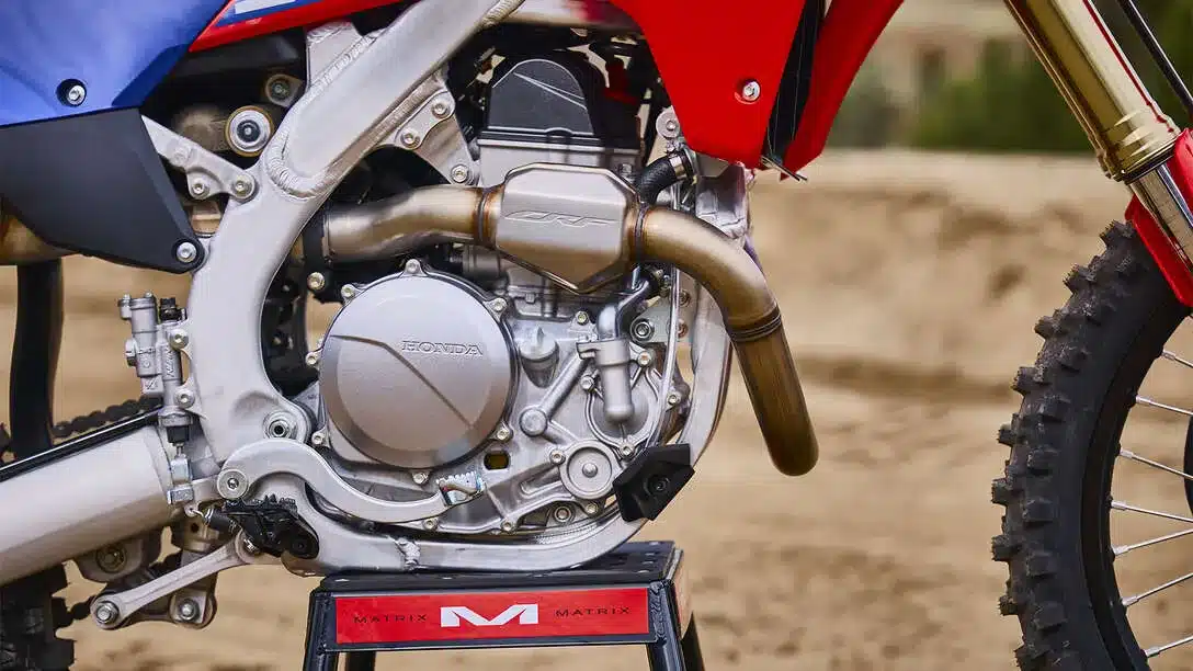 Motornahaufnahme der Honda CRF450R mit Rahmen, Fahrwerk und Auspuffanlage vor sandigem Streckenhintergrund