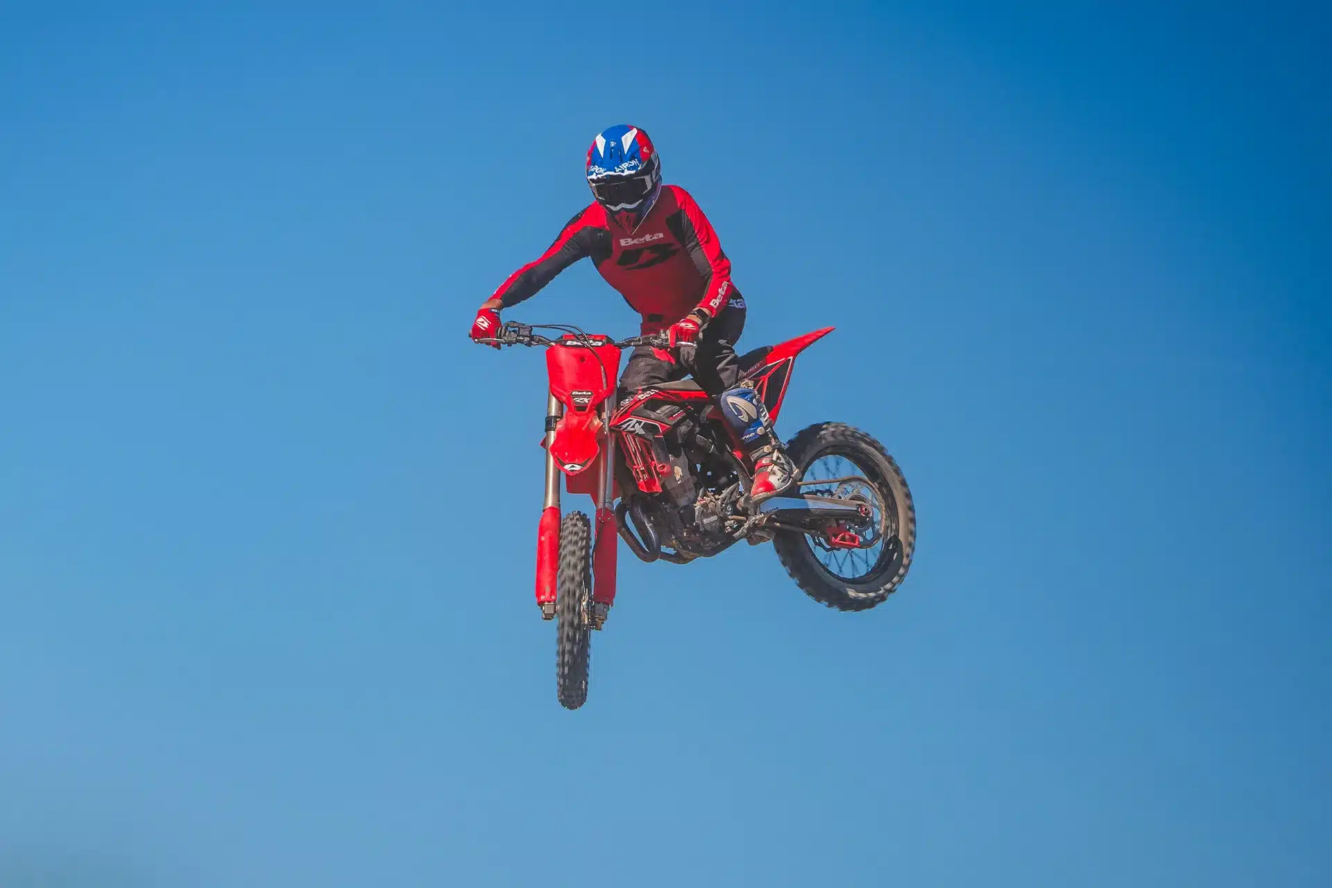 Motocross-Fahrer auf einer Beta RX 4T 450, Modelljahr 2027, beim Sprung vor blauem Himmel.