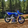 Yamaha YZ250 Motocross-Motorrad steht auf einer lehmigen Rennstrecke vor Waldkulisse.