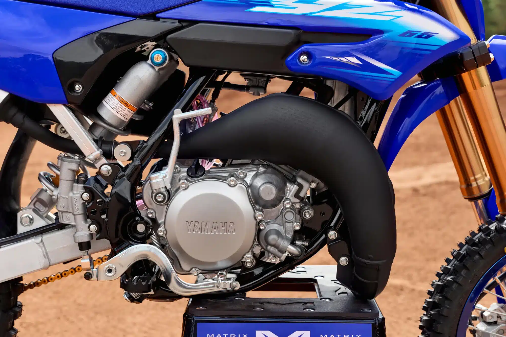 Nahaufnahme vom Motor, Auspuff und Fahrwerk der Yamaha YZ65 auf sandigem Untergrund