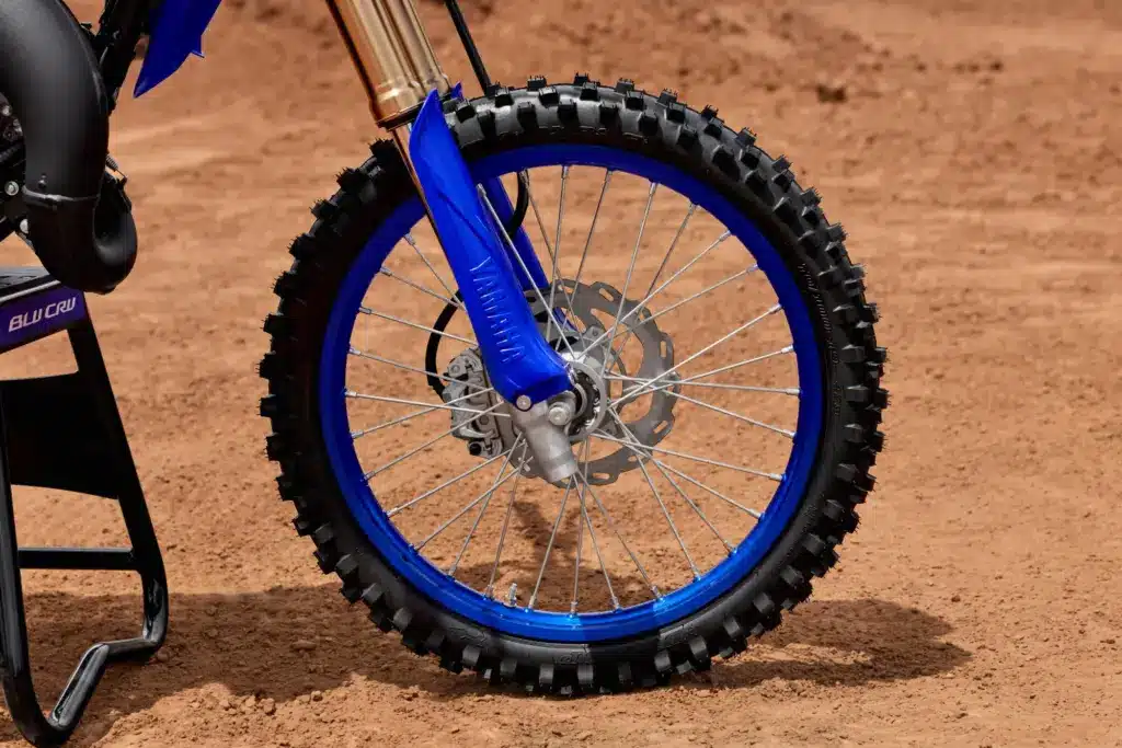 Vorderrad mit Scheibenbremse und Telegabel der Yamaha YZ85 auf sandigem Untergrund.
