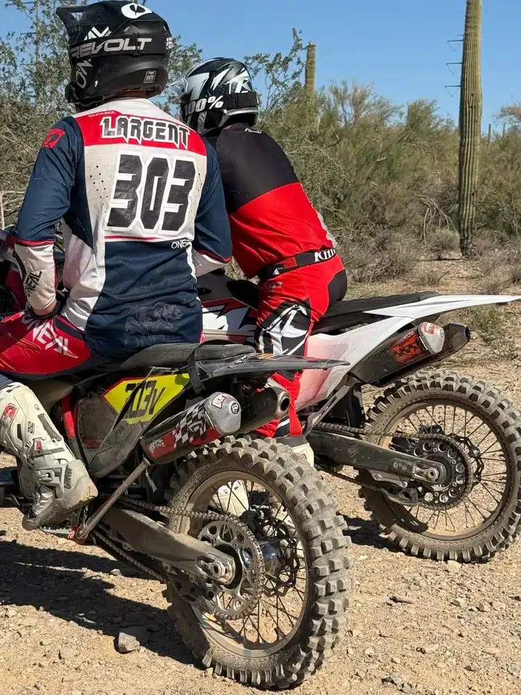 Zwei Offroad-Fahrer auf ihren Dirtbikes stehen nebeneinander im trockenen Wüstengelände