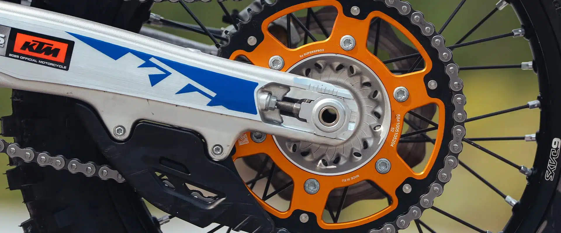Nahaufnahme des Hinterrads der KTM 350 EXC-F 6DAYS mit orangefarbenem Kettenrad und Kettenschutz.