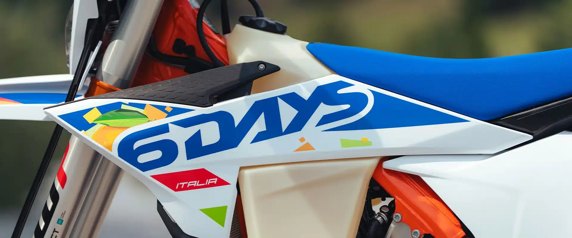 Detailfoto der KTM 300 EXC 6DAYS mit 6DAYS-Grafik, blauem Sitzbezug und orangefarbenem Rahmen.