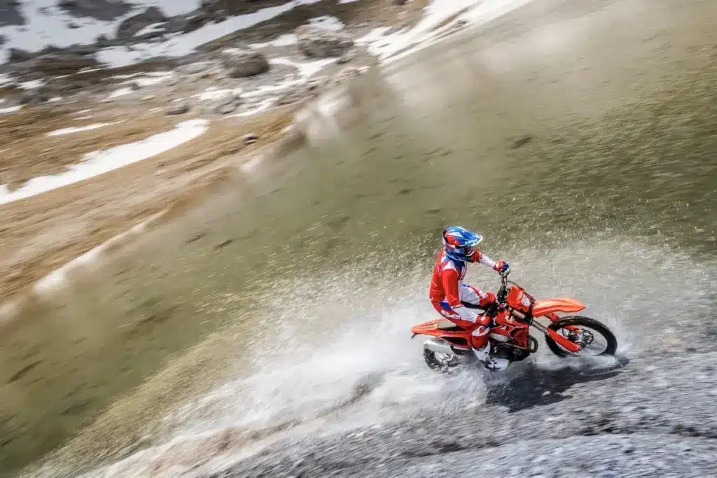Motorradfahrer auf einer Beta RR X-PRO 4T 390 fährt durch Wasser vor alpiner Kulisse.