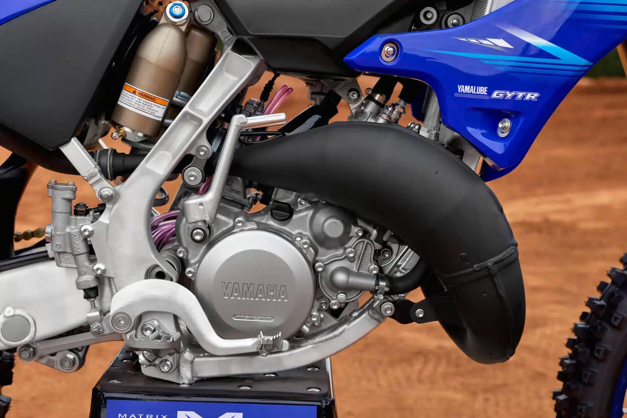 Nahaufnahme des Motors und Rahmens einer Yamaha YZ125 Motocross-Maschine auf sandigem Untergrund.