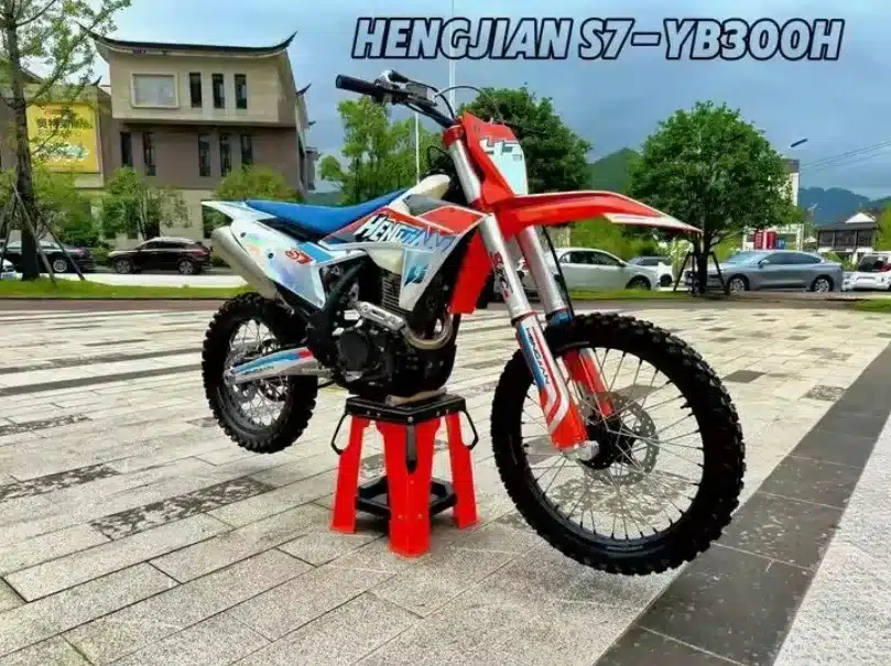 Die Hengjian S7-YBS300 steht auf einem Ständer, zeigt ihre geländetaugliche Bauweise mit grobstolligen Reifen, hoher Bodenfreiheit und sportlichem Design.
