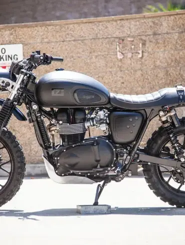 Seitliche Ansicht der Schlege Triumph Scrambler, individuell umgebaut mit schwarzem Design, groben Stollenreifen und minimalistischen Details
