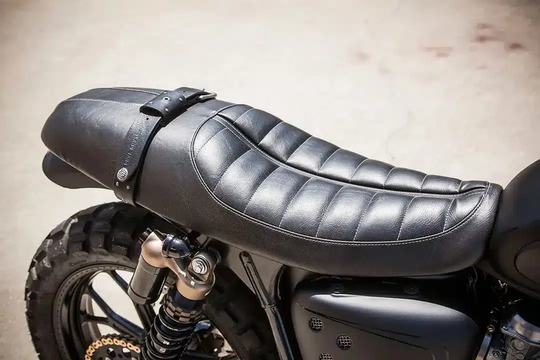 Detailaufnahme der schwarzen RSD Stepped Enzo Sitzbank auf einer Custom Scrambler Triumph mit grobstolligen Reifen.