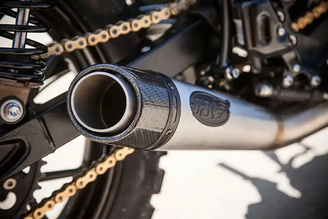 Nahaufnahme des Auspuffs der Schlege Triumph Scrambler mit sichtbaren Details von Kette, Federbein und Endrohr.