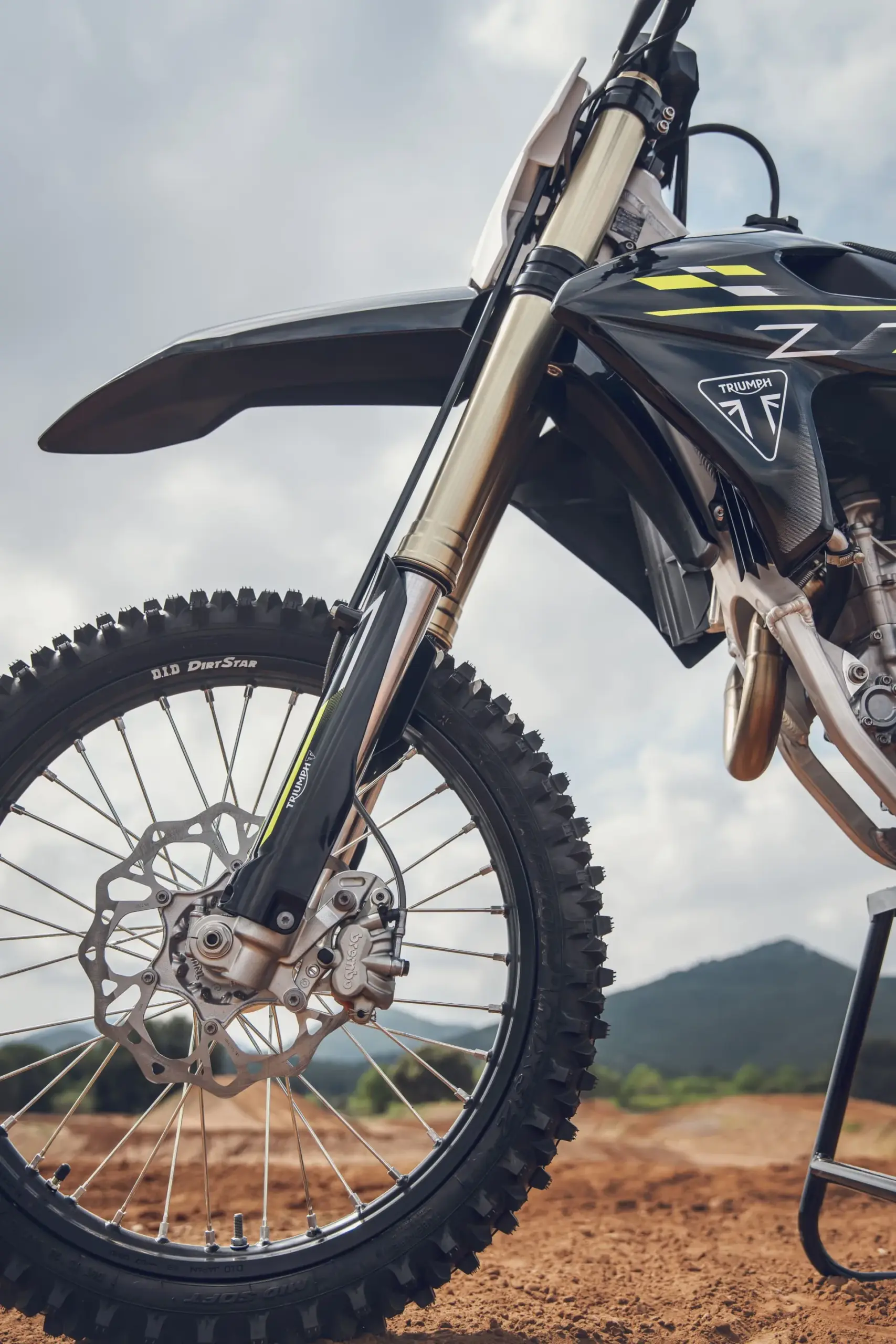 Nahaufnahme von Vorderrad, Bremse und Gabel der Triumph TF 450-X auf unbefestigtem Untergrund.