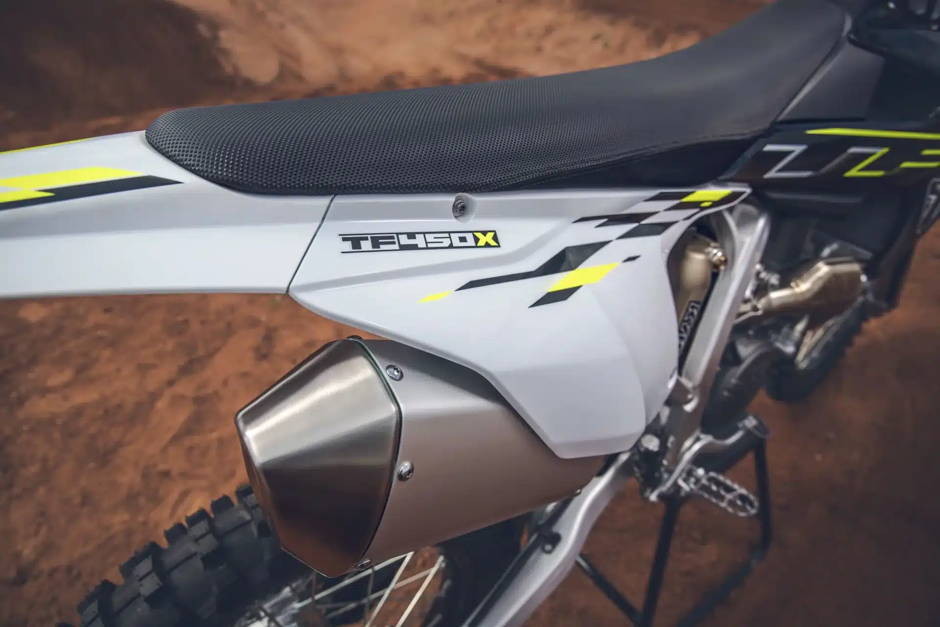Nahaufnahme des Seitenteils und Auspuffs der Triumph TF 450-X auf sandigem Untergrund