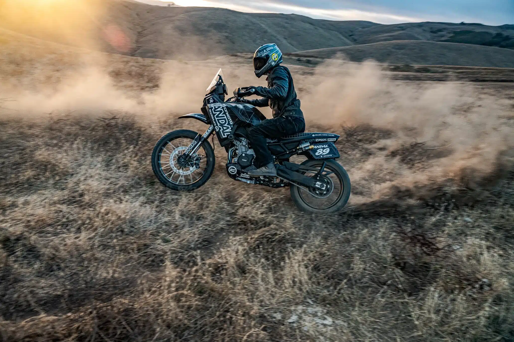 VANDAL 2 Adventure-Bike fährt durch trockenes, staubiges Gelände bei Sonnenuntergang.