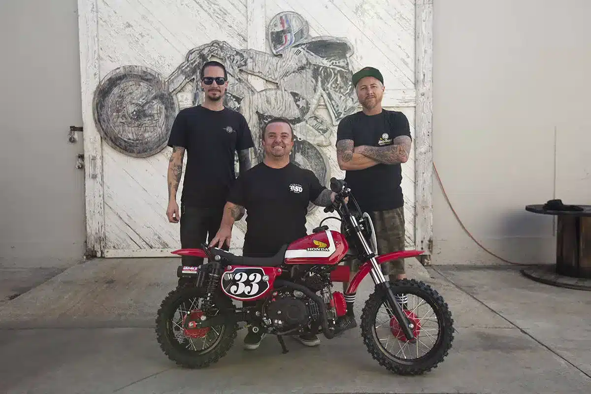 Honda Wee Man CRF110 Custom-Umbau mit drei Personen vor Garagentor