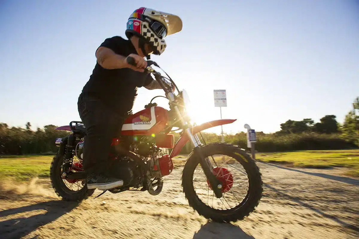 Wee Man CRF 110 Custom-Motorrad fährt auf Sandweg bei Sonnenschein