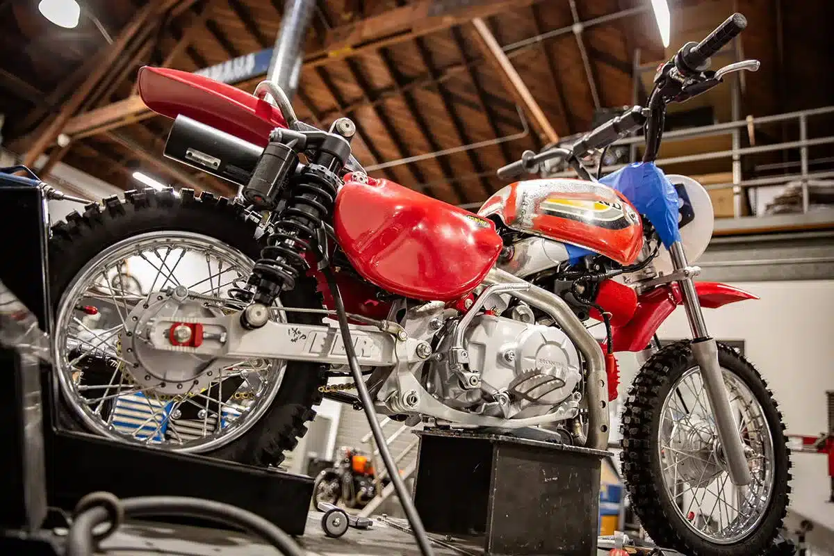 Seitenansicht eines individuell umgebauten Wee Man CRF 110 Motorrads mit rotem Tank und auffälligen Federbeinen.