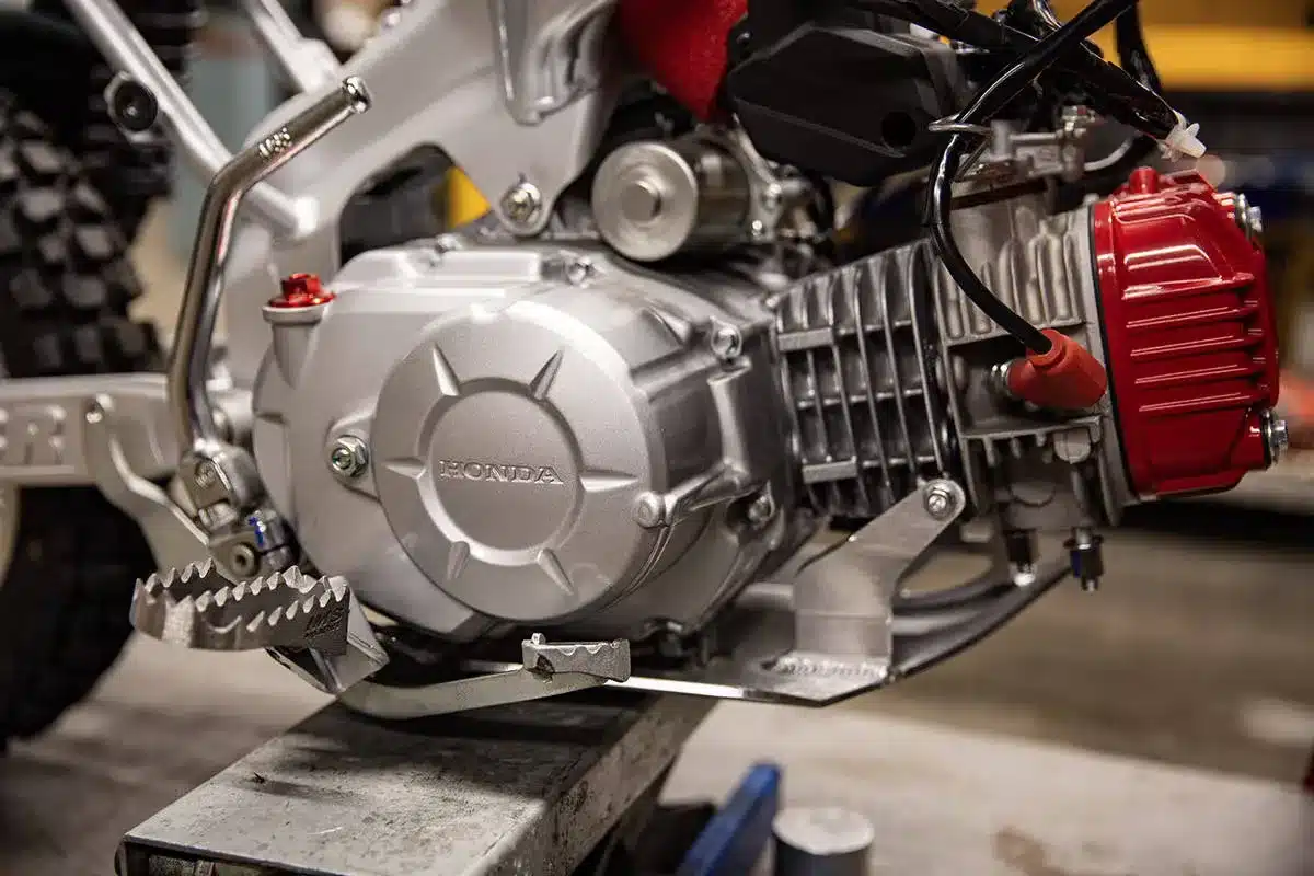 Nahaufnahme vom Motor der Wee Man Honda CRF 110 mit sichtbaren Umbauten und Fußraste.