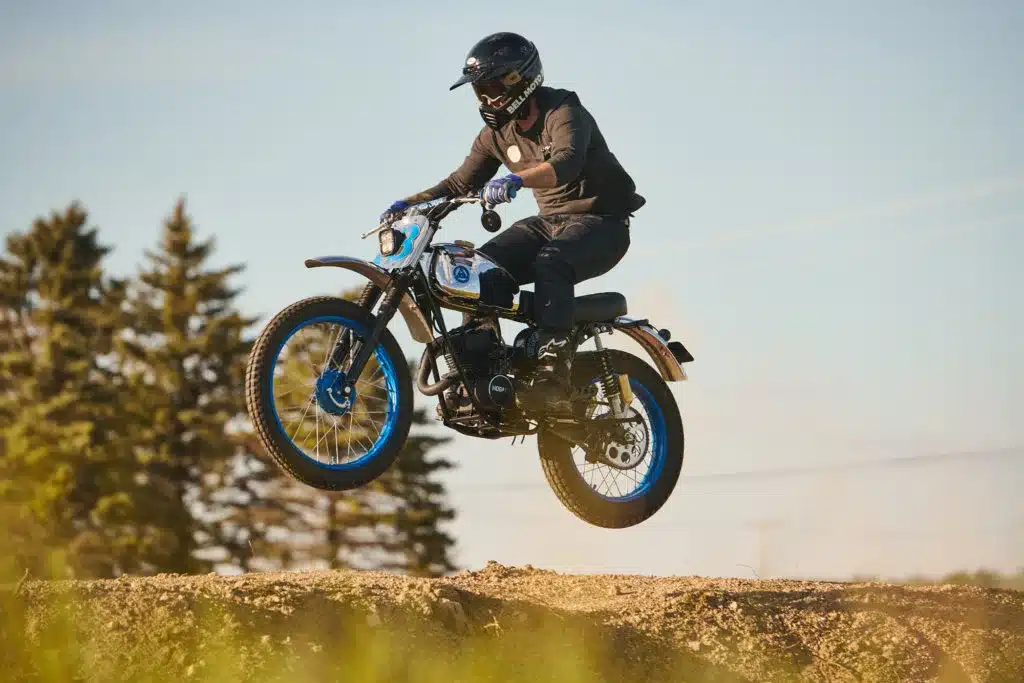 Motorradfahrer springt mit einer blauen Hodaka Wombat Blue Wombat über einen Hügel im Gelände.