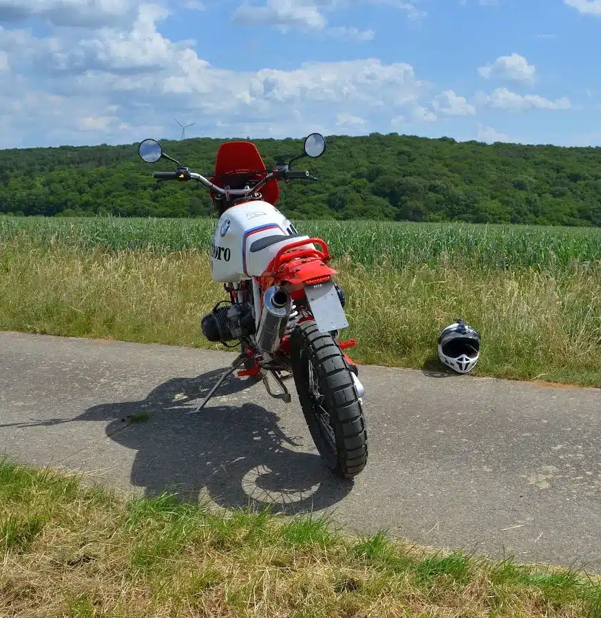 SWT-SPORTS EnduroBoxer Nr. 133, ein individuell umgebauter BMW-Boxer im Rallye-Stil, steht auf einem Feldweg, im Hintergrund Felder und Wald.