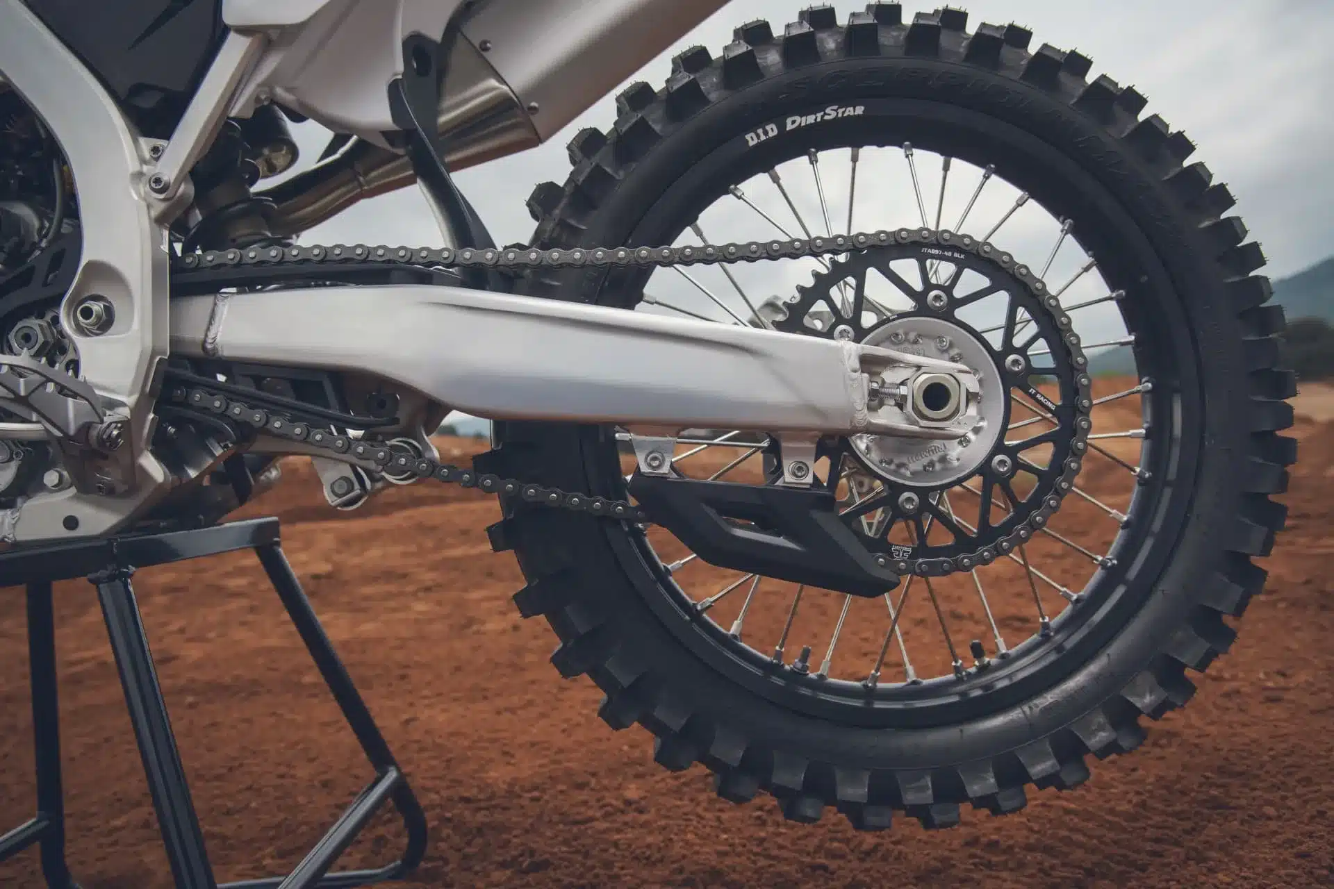 Nahaufnahme des Hinterrads und Antriebs einer Triumph TF 250-X mit D.I.D DirtStar-Felge und Pirelli MX32-Reifen auf rotem Motocross-Boden.