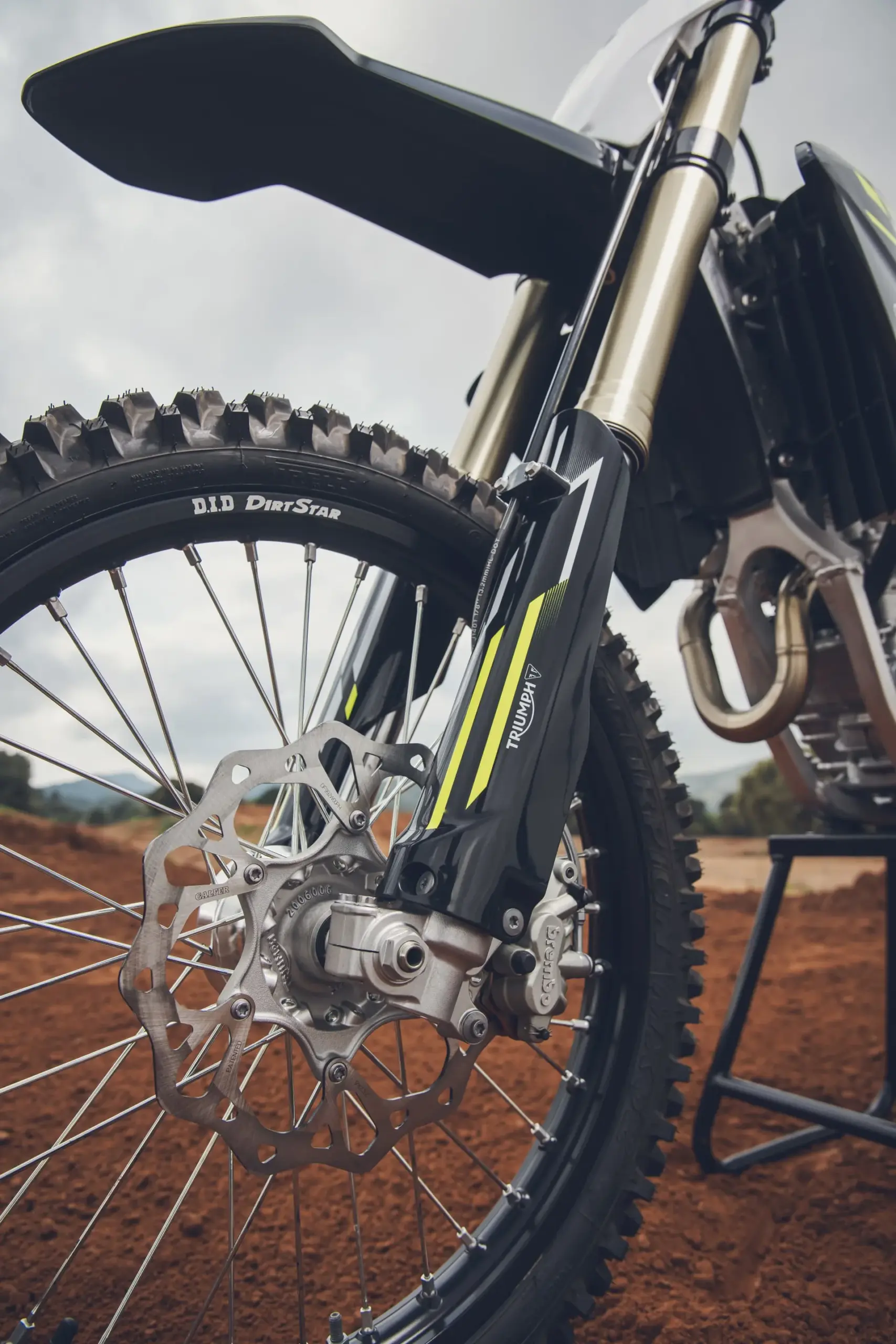 Detailaufnahme des Vorderrads, der Bremsanlage und der Gabel der Triumph TF 250-X auf einer Motocross-Strecke.