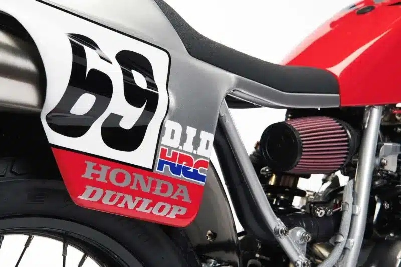 Detailaufnahme des Hecks einer umgebauten Honda XR650L mit Startnummer 69, sichtbarem Luftfilter und typischen Sponsorenaufklebern.