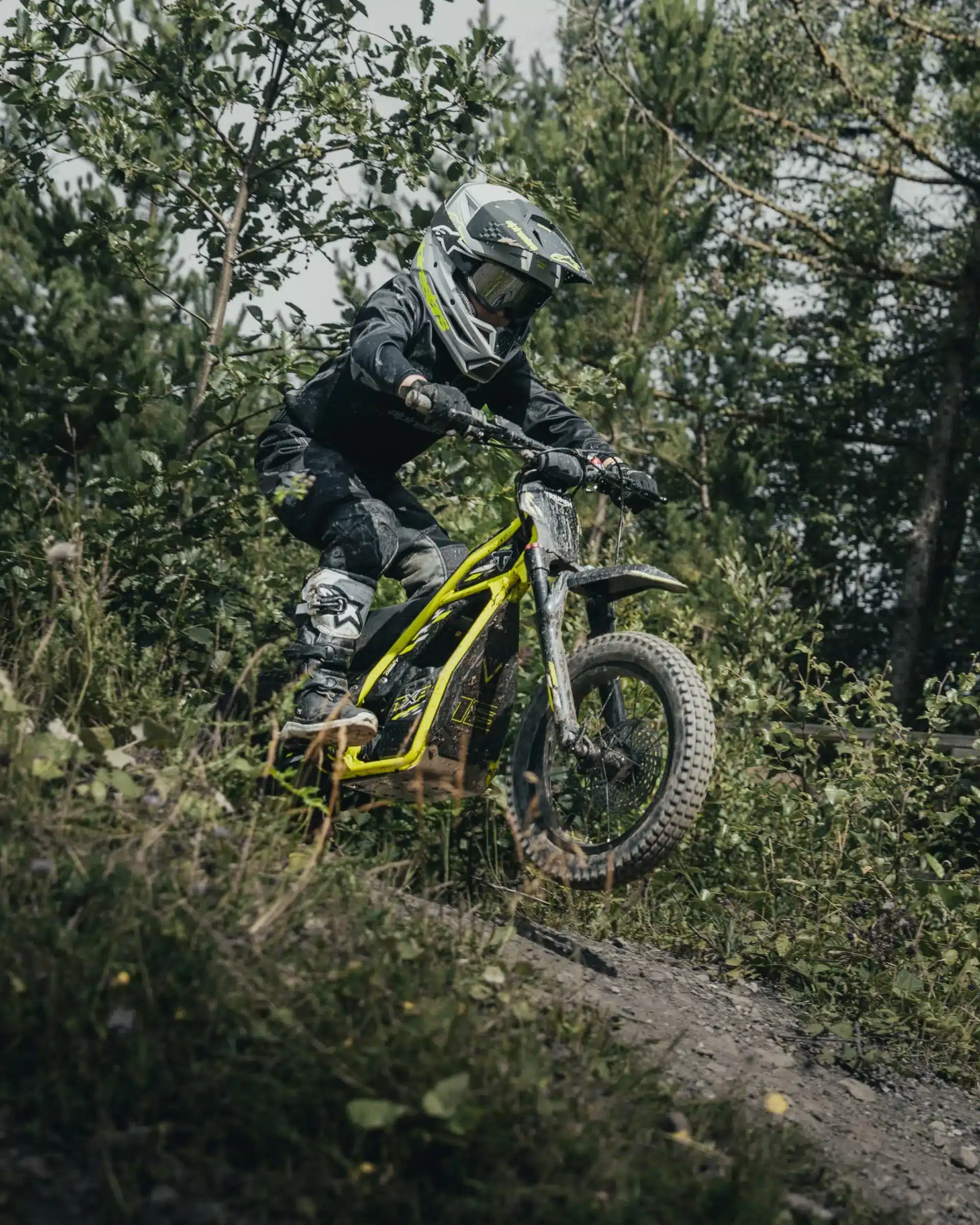 Ein Kind fährt die Triumph TXP-16, ein elektrisches Offroad-Motorrad, durch ein Waldstück.