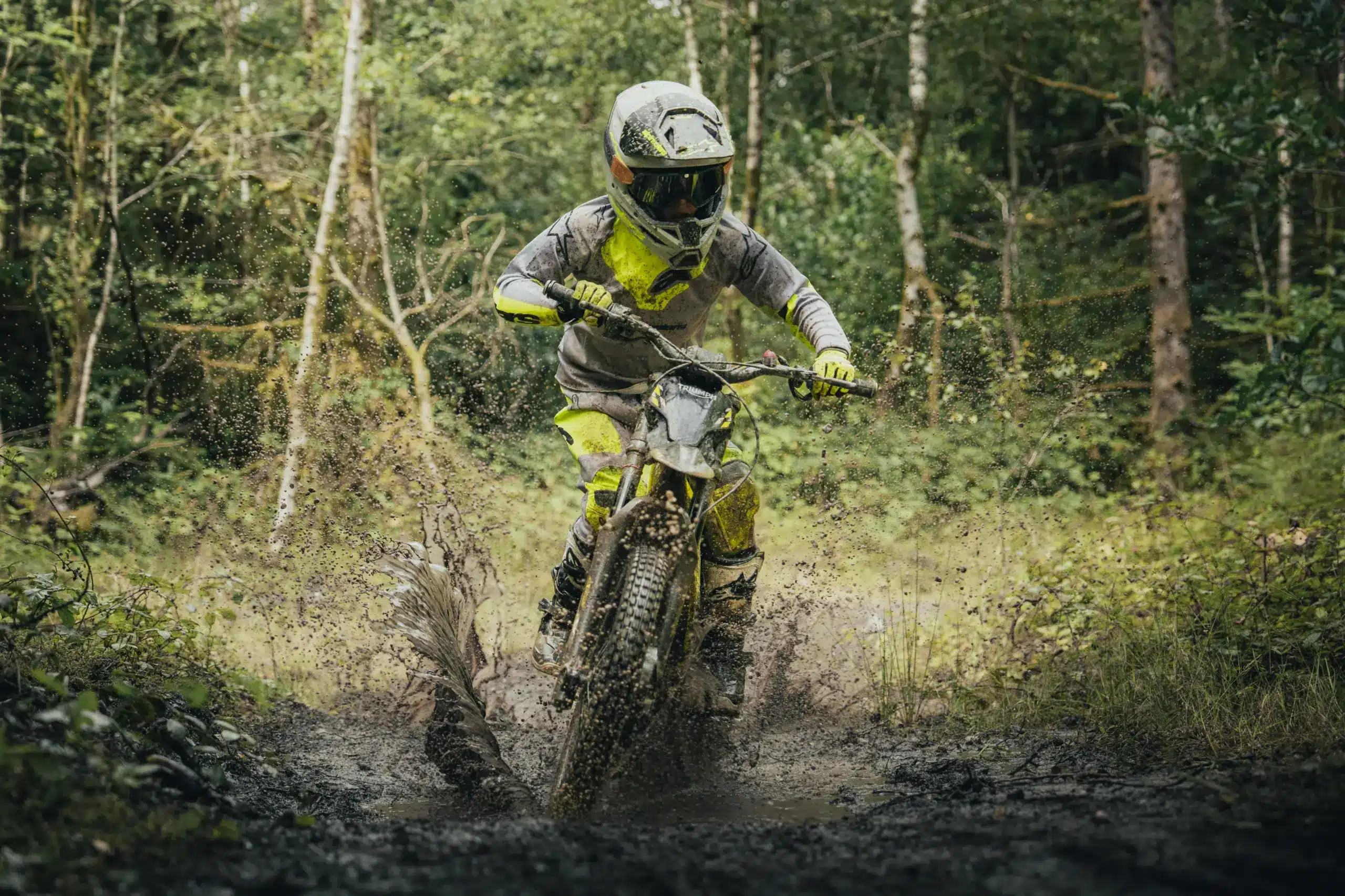 Junger Fahrer auf einer Triumph TXP-20 fährt durch eine matschige Pfütze im Wald