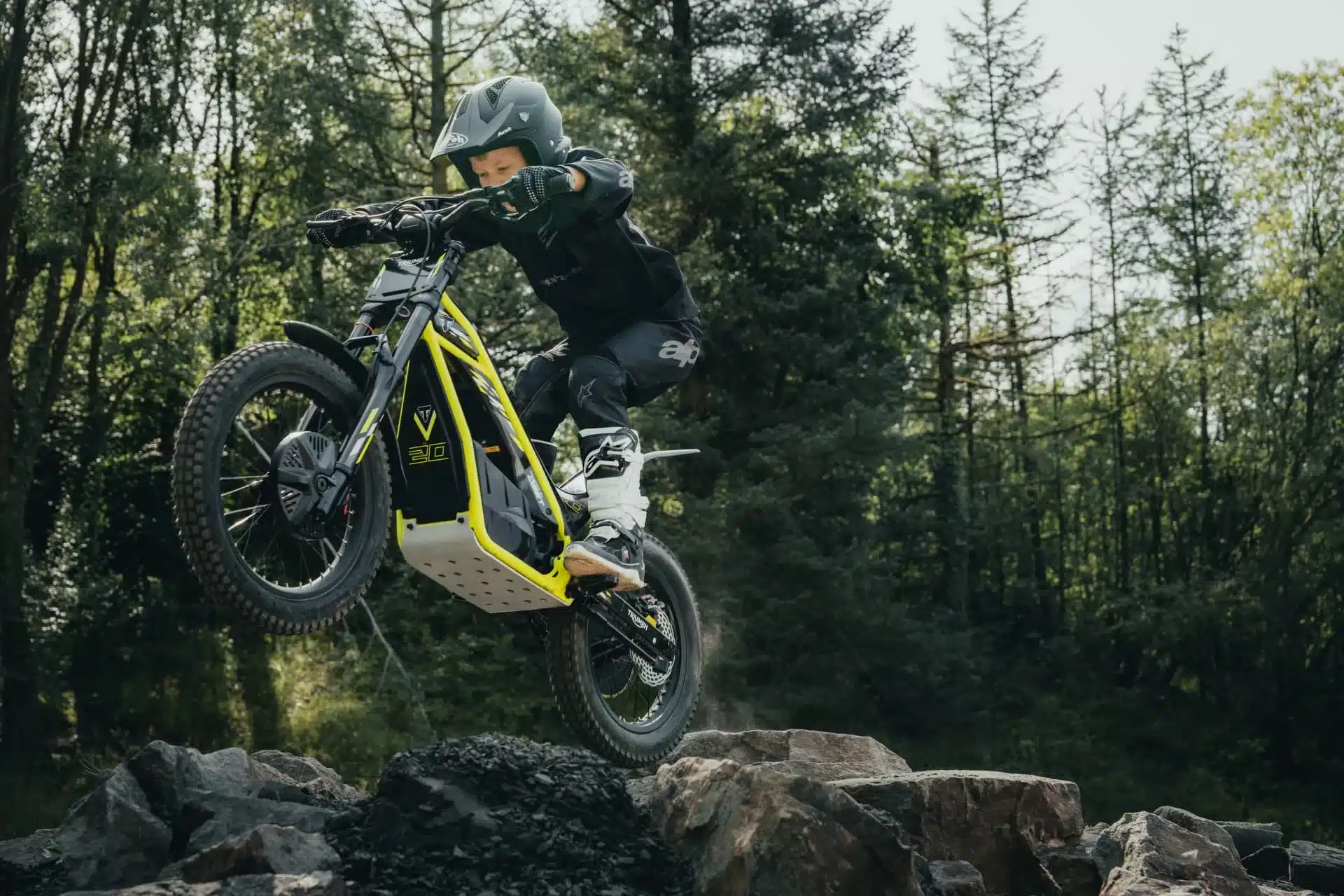 Kind auf elektrischem Offroad-Motorrad Triumph TXP-20 beim Überwinden von Felsen
