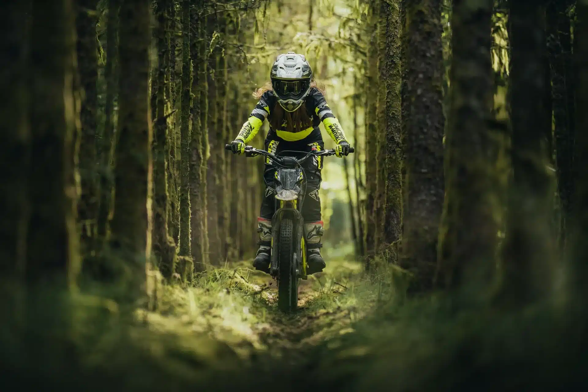 Triumph TXP-24 Elektromotorrad im Gelände zwischen Bäumen, frontal aufgenommen