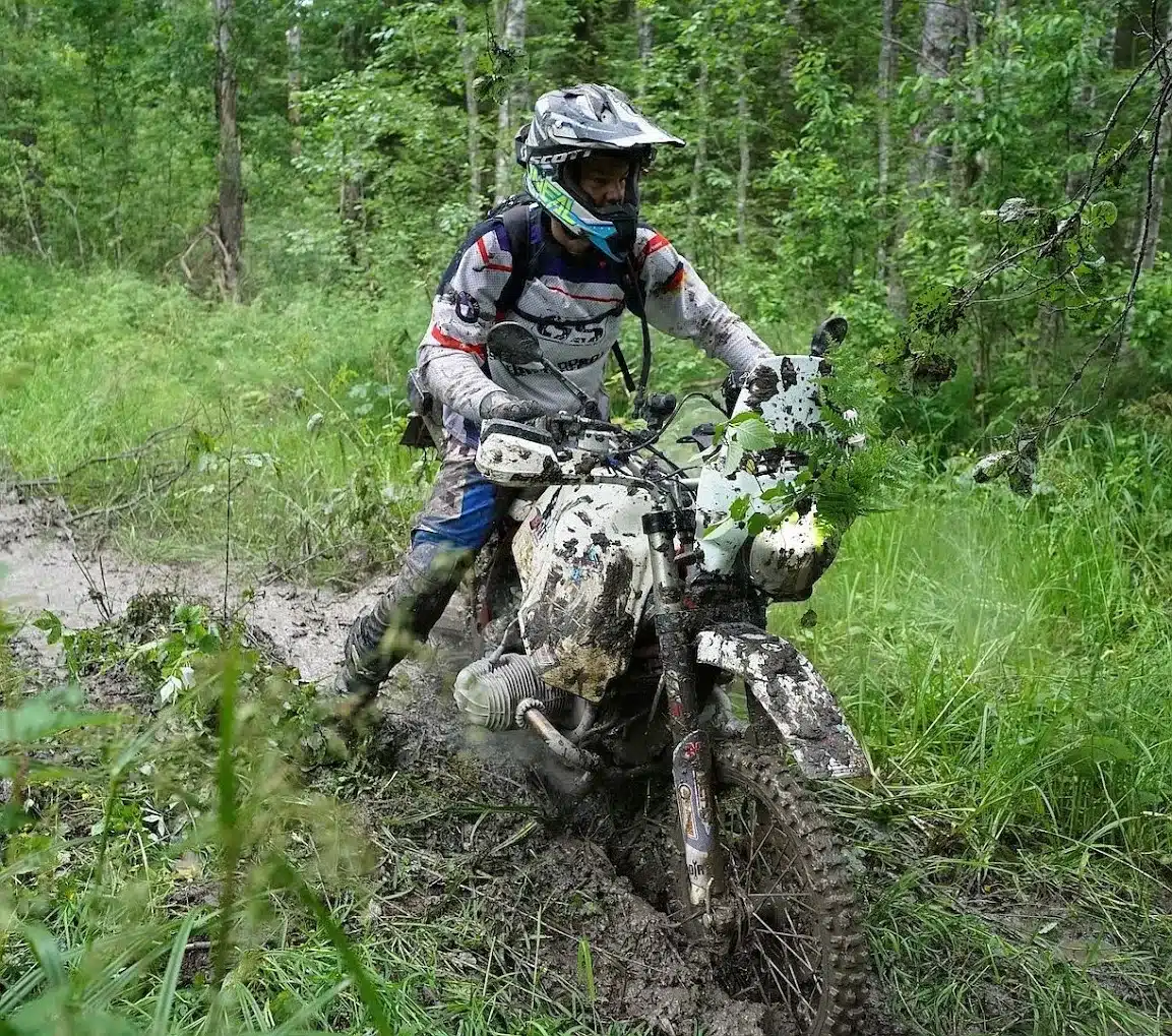 Motorradfahrer auf stark verschlammter BMW R 100 R Geländeumbau im Wald abseits befestigter Wege.